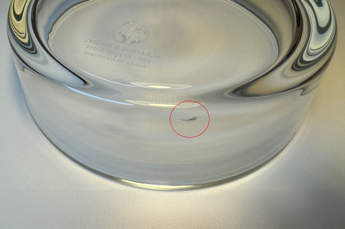 Detailed close-up of the back of a glass drinking bowl for cats with a manufacturing defect, marked with a red circle – view from above at an angle