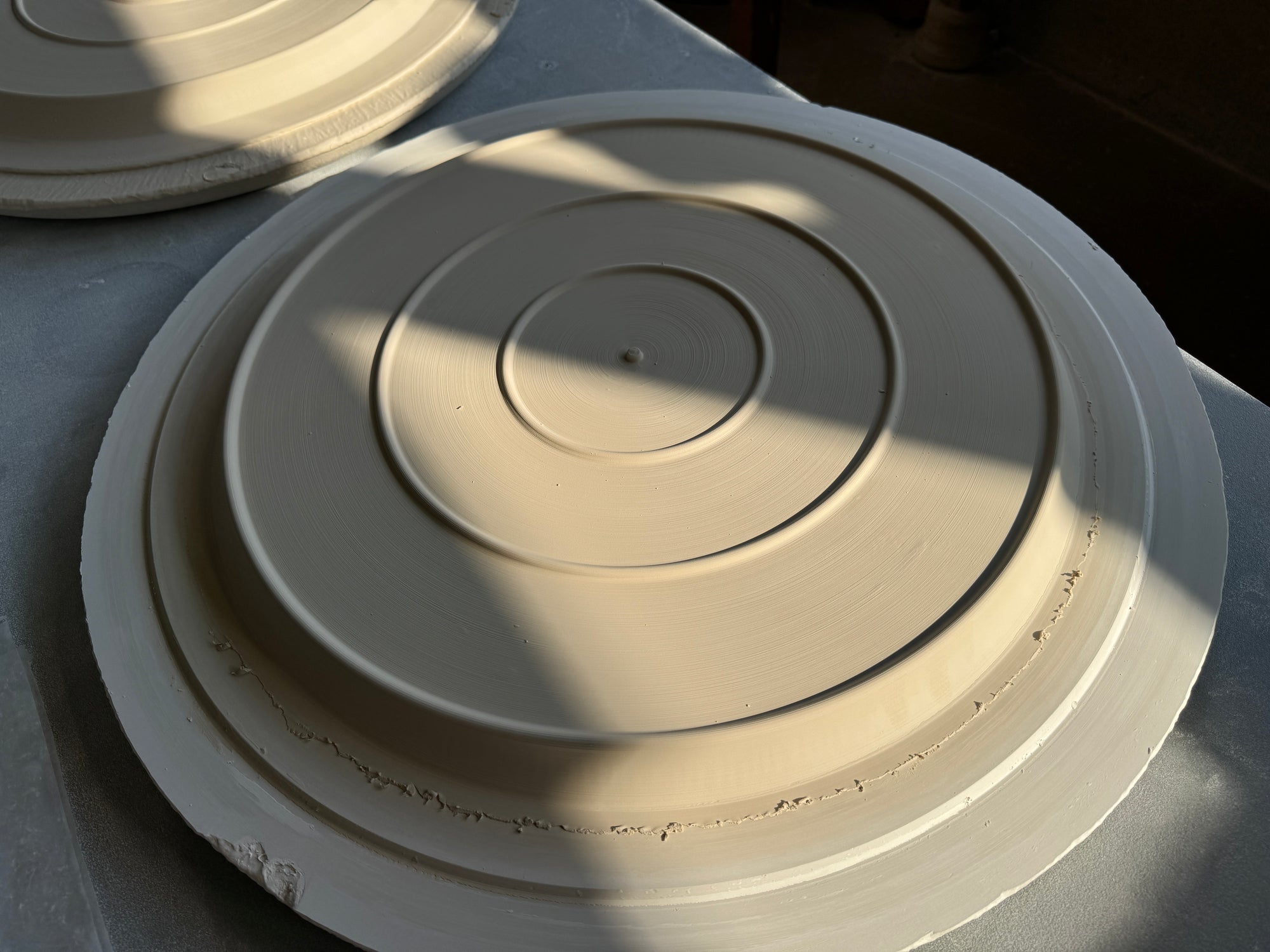 Underside with three base rings of a large cat plate made of unfired porcelain raw material on a turntable