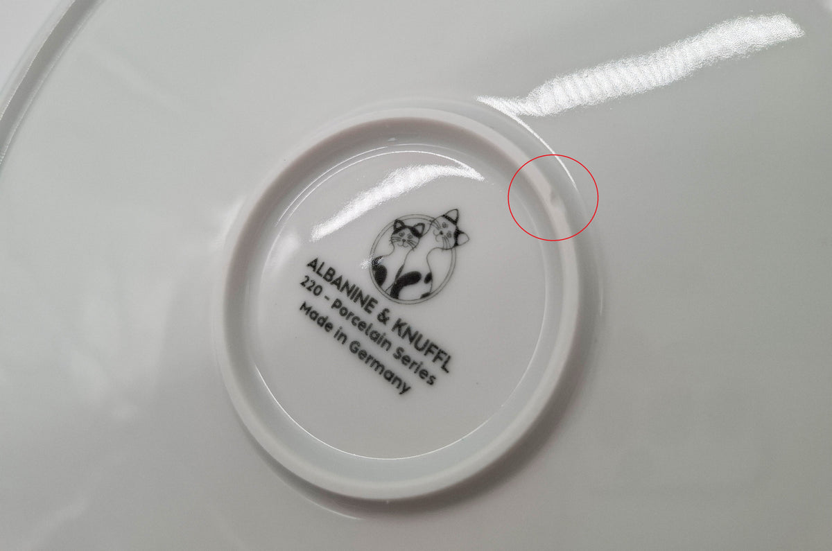 Ausschnitt Nahaufnahme Rückseite Katzenteller mit Logo und durch kleinen Ausbruch beschädigtem Bodenring – gekennzeichnet durch roten Kreis