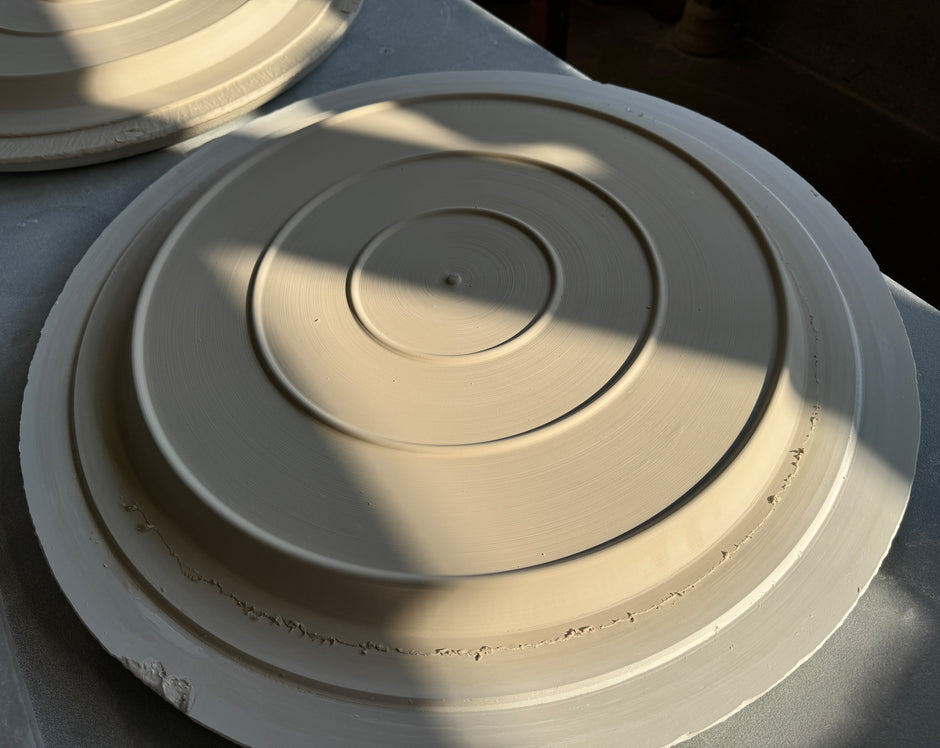Underside with three base rings of a large cat plate made of unfired porcelain raw material on a turntable